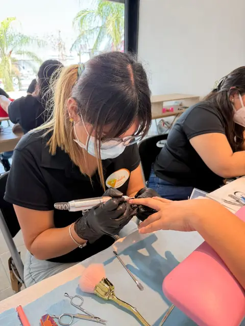 Alumna usando el drill sobre la uña de su modelo